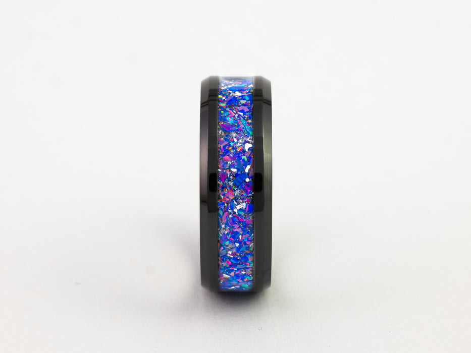 Side view of black tungsten ring with purple-blue crushed opal inlay on white background.