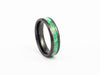 Angled studio shot of the Black Ceramic Ring with bright green fire opal flake inlay on white background.