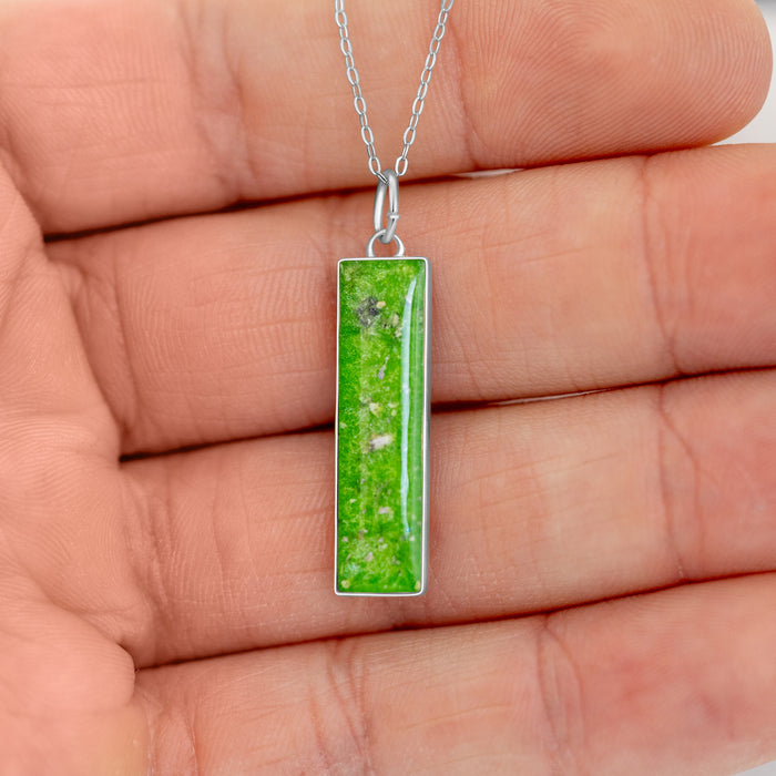 Hand holding a sterling silver bar pendant with vibrant lime green resin and shimmering silver flakes.