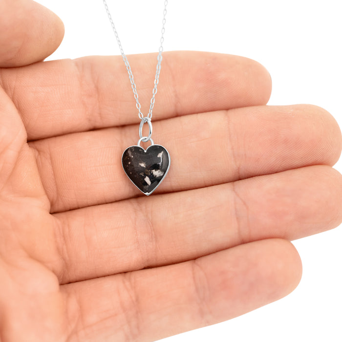 Sterling silver heart pendant with black resin and silver flakes, shown worn in a hand for details.
