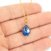 Gold-plated teardrop pendant with blue resin and silver flakes, shown worn in the palm of a hand for scale.