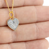Close-up photo of a hand holding a gold-plated heart pendant with white/gray resin and subtle dark speckles.