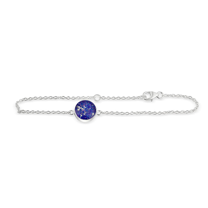 Thin sterling silver chain bracelet featuring a round charm with a bright blue opal resin inlay and silver flakes.