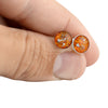 Close-up of a hand holding two sterling silver stud earrings featuring round vibrant orange and gold opal resin inlays.