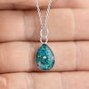 Close-up photo of a hand holding a sterling silver teardrop pendant with vibrant teal blue resin and internal silver flake accents.