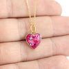 Close-up photo of a hand holding a gold-plated heart pendant with vibrant pink resin and shimmering silver flakes