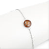 Thin sterling silver chain bracelet featuring a round charm with a brown resin inlay accented by gold and silver flakes.