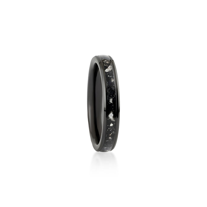 Close-up of a hand holding a thin black band ring with a continuous black resin inlay and white and silver flakes.