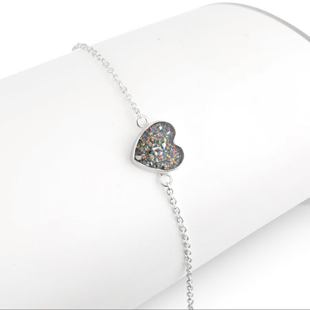 Silver chain bracelet displayed on a white stand, featuring a heart-shaped charm inlaid with multicolored opal resin.