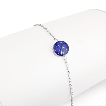 Silver chain bracelet displayed on a white stand, detailed with a round, bright blue opal resin charm.