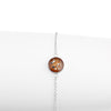 Thin sterling silver chain bracelet featuring a round charm with a brown resin inlay accented by gold and silver flakes.
