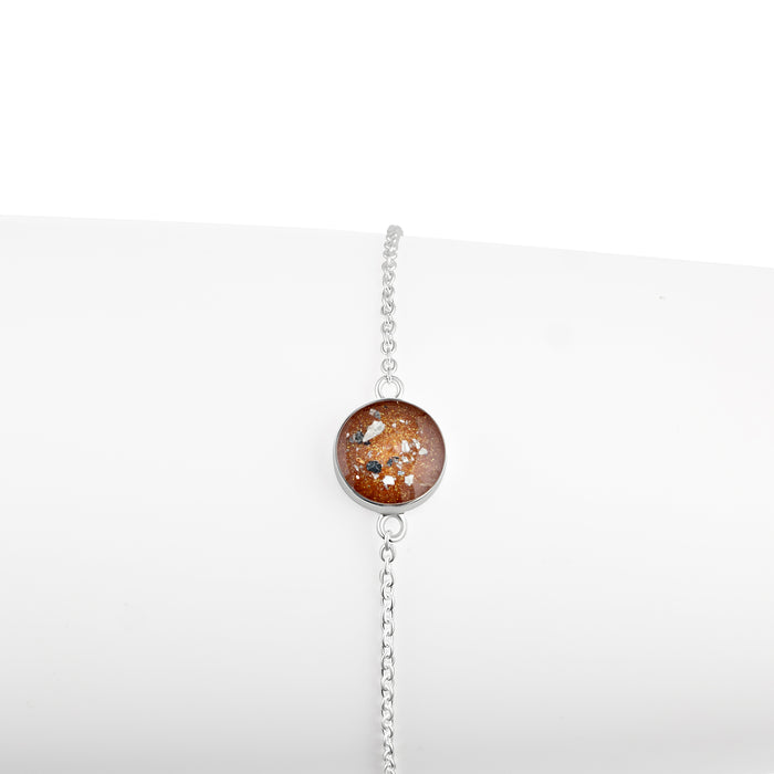 Thin sterling silver chain bracelet featuring a round charm with a brown resin inlay accented by gold and silver flakes.