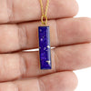 Hand holding a gold-plated bar pendant with vibrant blue resin and shimmering silver flakes.
