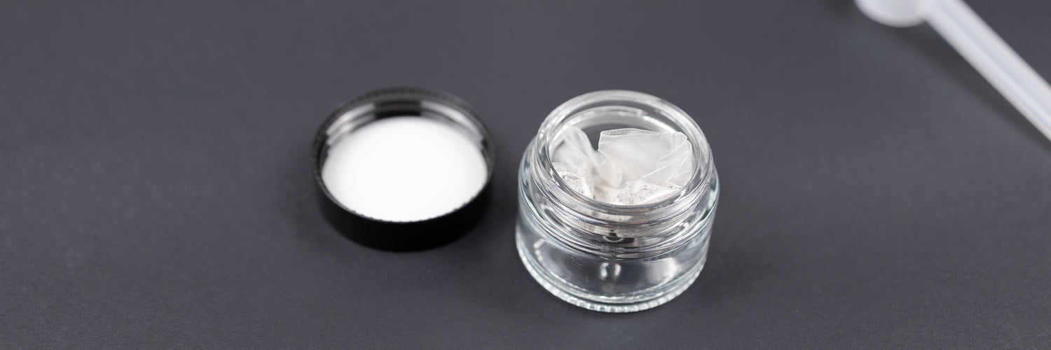 Close-up overhead view of a small glass jar containing cremation ashes material and a loose lid.