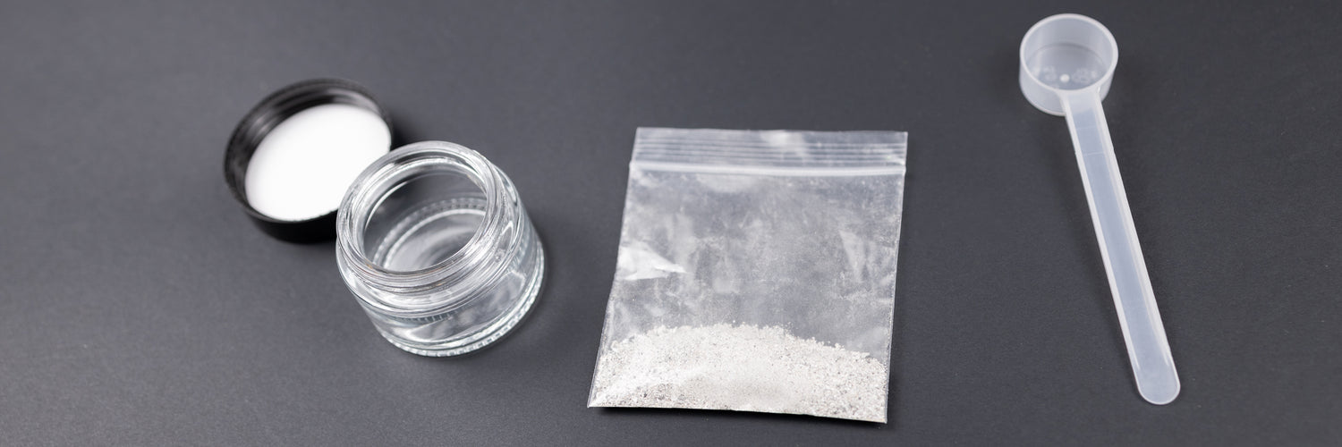 Close-up of cremation ashes material in a small plastic baggie, next to a jar and scoop.