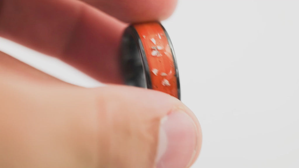 360-degree view detail of the Black Ceramic Ring with orange and Mother-of-Pearl inlay, held in hand.