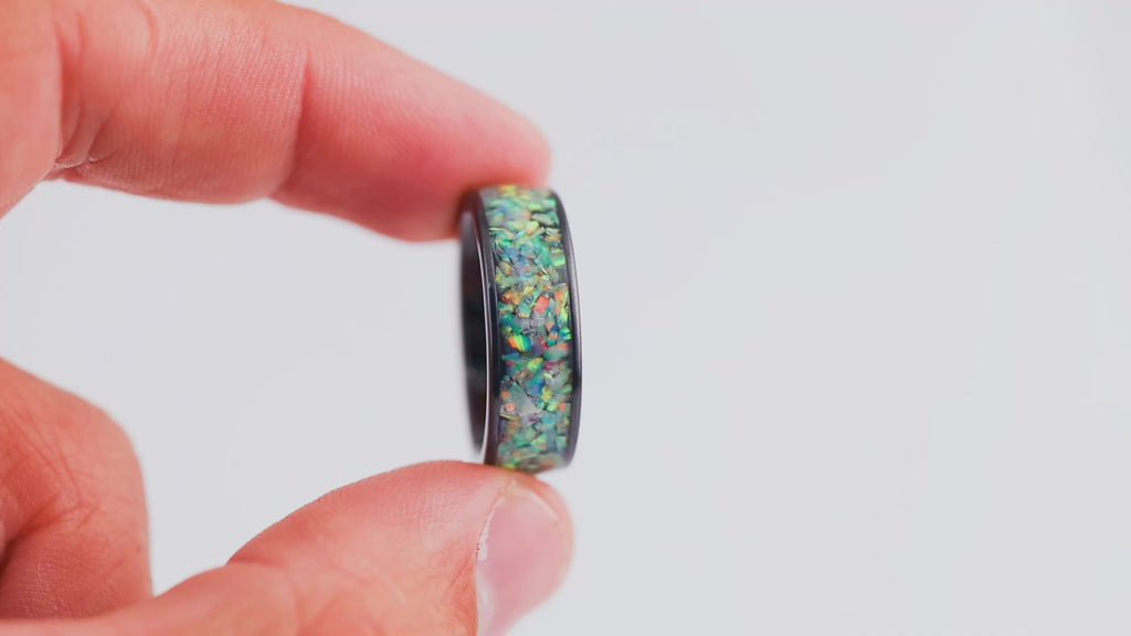 Demonstration video showing a hand holding and rotating a wide black band ring with multicolored opal resin inlay.