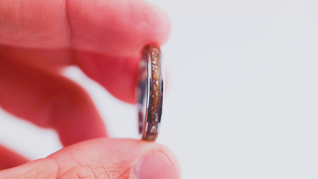 Video showing a hand holding and rotating a thin silver band ring with brown resin and gold fleck inlay.